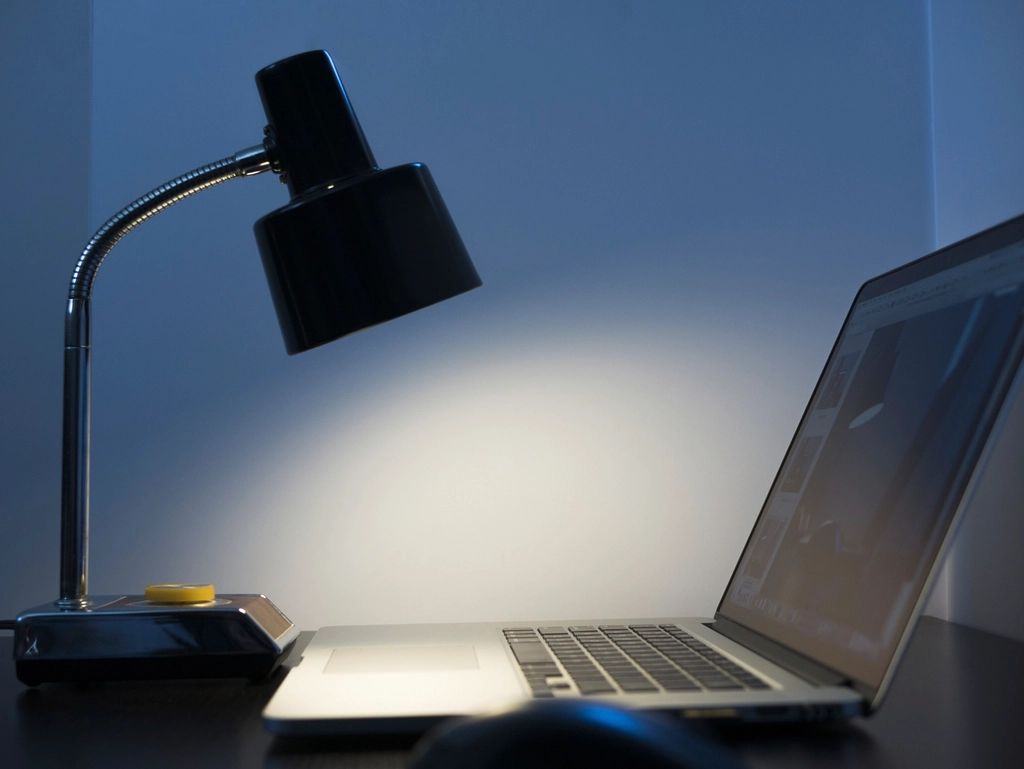 Luminária acesa sobre notebook numa mesa de trabalho